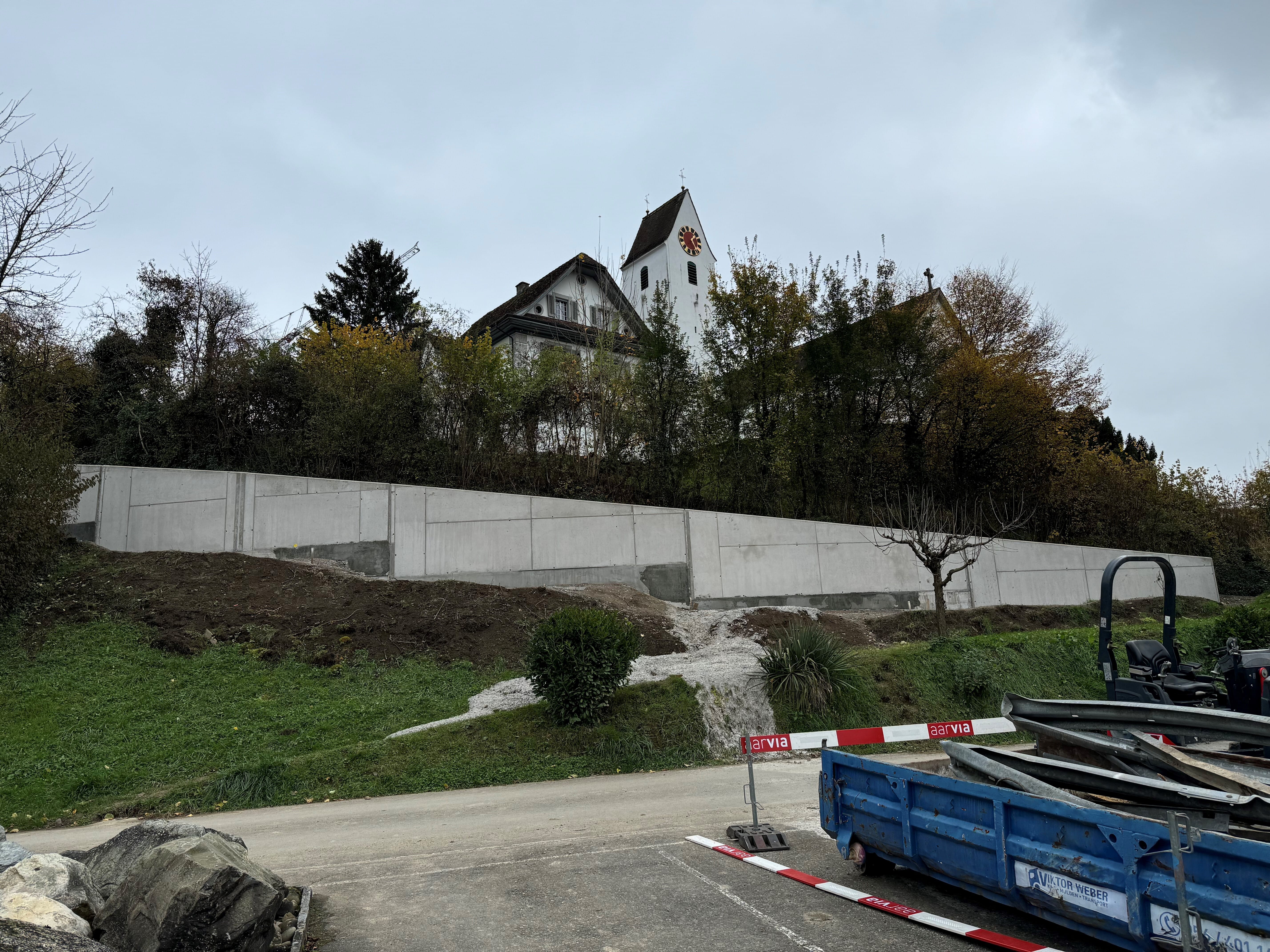 Projekt «Ausbau & Sanierung Kirchrainstrasse & EW-Rohrblock Im Rebhügel» – noch nicht hinterfüllte Stützmauer der Kirchrainstrasse am 13.11.2024. Nach der talseitigen Böschung wird von der Stützmauer in der Höhe noch etwa 90 Zentimeter zu sehen sein. Zum Schluss wird die sichtbare Oberfläche im Einvernehmen mit der kantonalen Denkmalpflege im Sponge-Jet-Strahlverfahren behandelt, um die Mauer möglichst optimal in die Umgebung der denkmalgeschützten Kirchengruppe zu integrieren. Bild: GK Eggenwil/Gemeindeschreiber Walter Bürgi