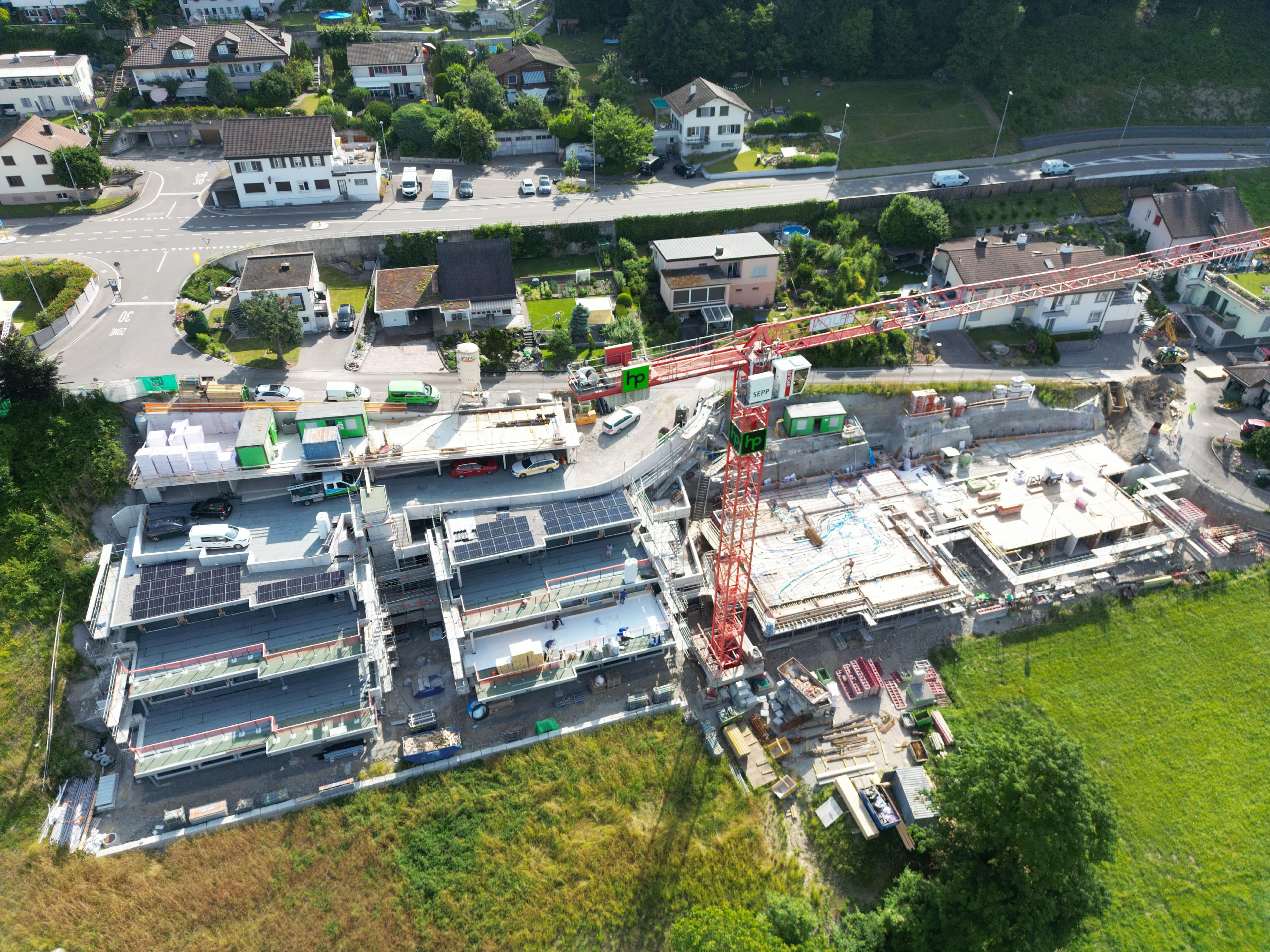 Aufgrund der Fertigstellungsarbeiten am nördlichen Parkdeck 1 der Terrassenhausüberbauung Erlismatt (links oben im Bild) ist bis Mitte Oktober 2025 mit einem erhöhten Aufkommen von parkierten Handwerkerfahrzeugen auf der Pflanzerfeldstrasse und am Erlismattweg zu rechnen. Sobald die Isolations- und Belagsarbeiten beim Parkdeck abgeschlossen sind, können dort wieder innerhalb der Baustelle Fahrzeuge abgestellt werden. Gemeindebehörde und Bauherrschaft bitten die Anwohner und Verkehrsteilnehmenden um Nachsicht für unvermeidbare Behinderungen oder Unannehmlichkeiten und danken für das Verständnis. Drohnenbild: Architekt Alex Müller/23.06.2025