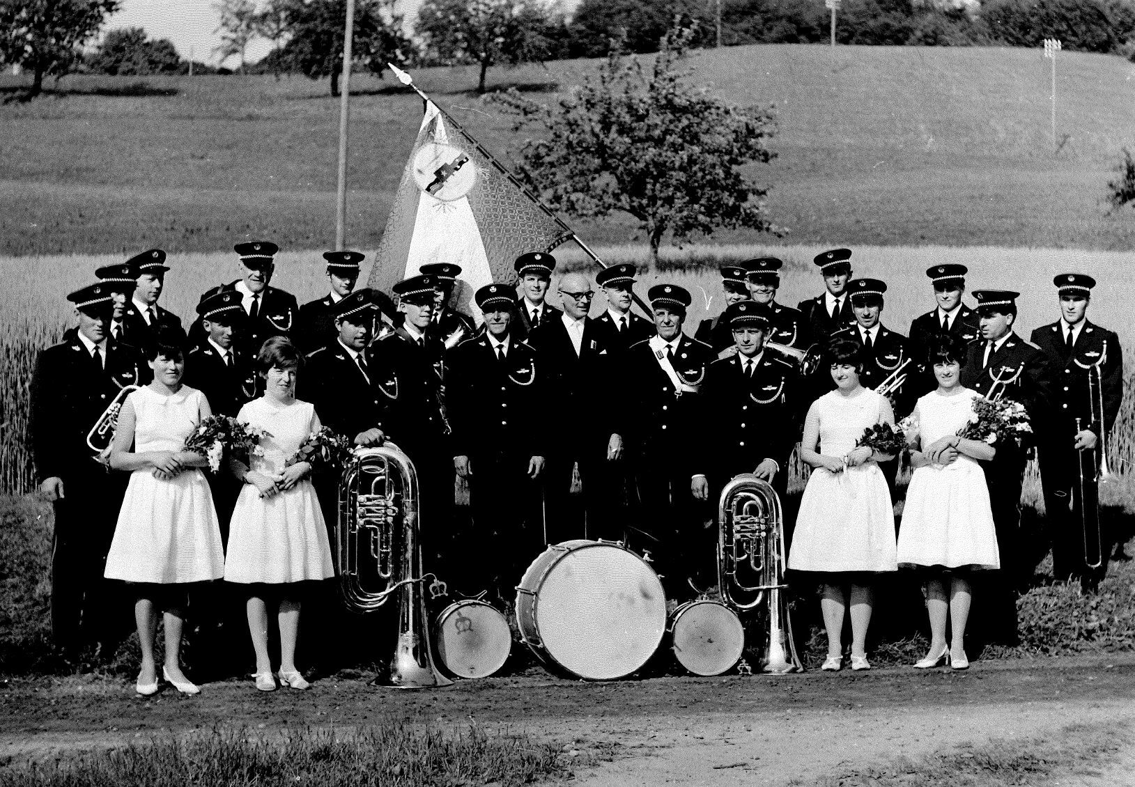 Bild der Musikgesellschaft Eggenwil bei der Uniformweihe 1967 in Eggenwil von H. Dubler, Arni. Die handschriftliche Bildlegende (wer ist wer?) samt Zeitungsbericht kann hier abgerufen werden. Auszug aus der damaligen Medienberichterstattung: «Nachher folgte die Festrede von Gemeindeammann Fridolin Müller, flankiert von je zwei «Dorfschönsten» zur Rechten und zur Linken. Einleitend begrüsste er die Ehrengäste, Veteranen und Gastsektionen. Den Initianten der neuen Uniform gratulierte er im besonderen für ihren Unternehmungsgeist. Der Redner erinnerte unter anderem an die Gründung der Musikgesellschaft Eggenwil im Jahre 1926 sowie an die Weihe der alten, feldgrauen Uniform im Jahre 1939. Sie versah also während 28 Jahren ihre Dienste. Wir wollen und dürfen Stolz auf das neue, wohlgelungene Werk sein, auf unsere Uniform, dies aber im Bewusstsein des Fortbestehens eines echten und guten Kameradschaftsgeistes. In ermunternden Worten schloss Gemeindeammann Müller seine kurze, prägnante Rede: «Schulter an Schulter, Herz an Herz, wollen wir zuversichtlich in die Zukunft blicken und auf gute Zusammenarbeit im Verein und in der Gemeinde bedacht sein!»