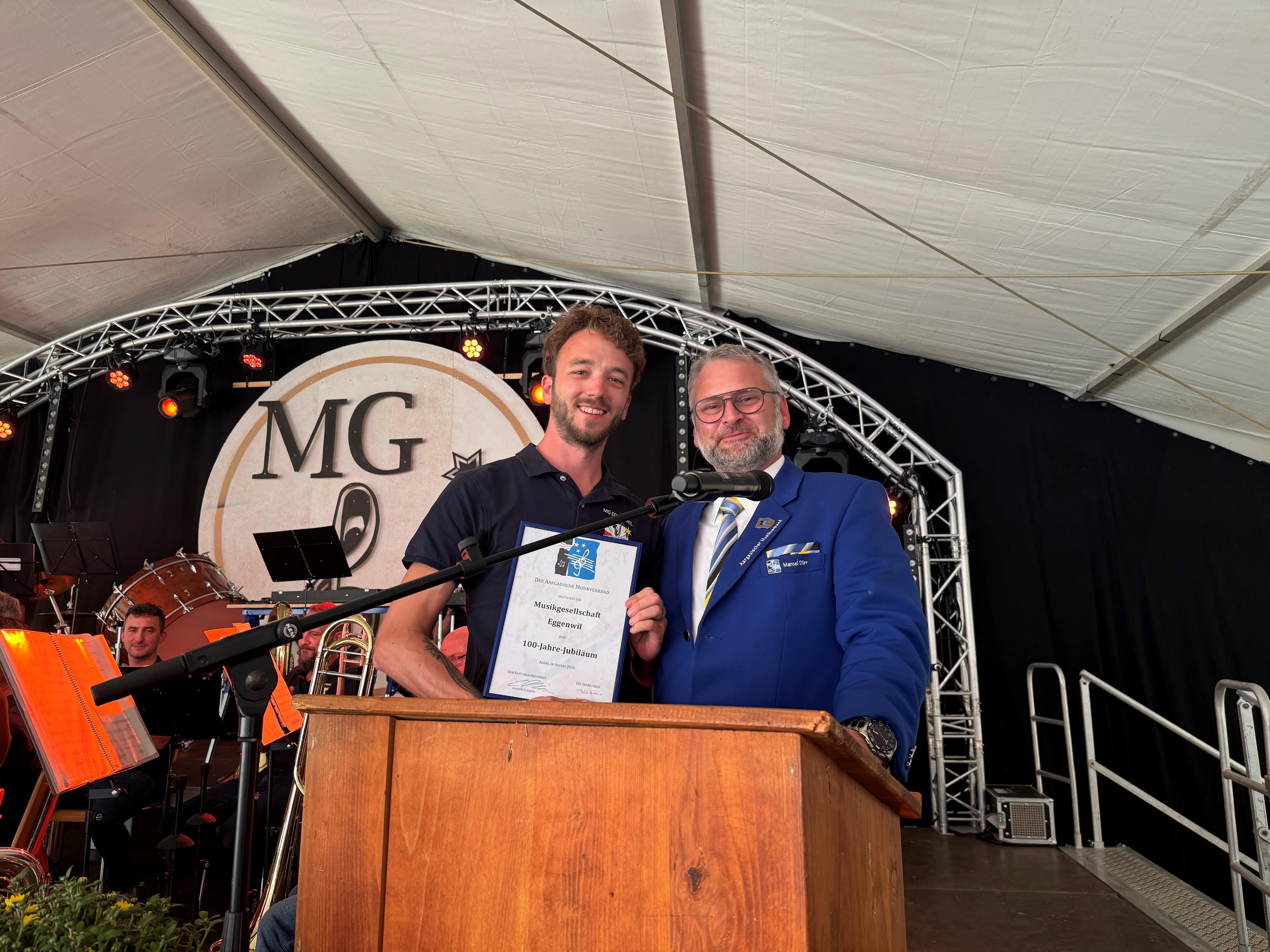 Nach seinem herzlichen Grusswort überreichte Marcel Dürr im Namen des Aargauischen Musikverbands der Musikgesellschaft Eggenwil, vertreten durch Yannick Meier, die Gratulations-Urkunde zum 100-Jahre-Jubiläum. Bild: Walter Bürgi/22.08.2026